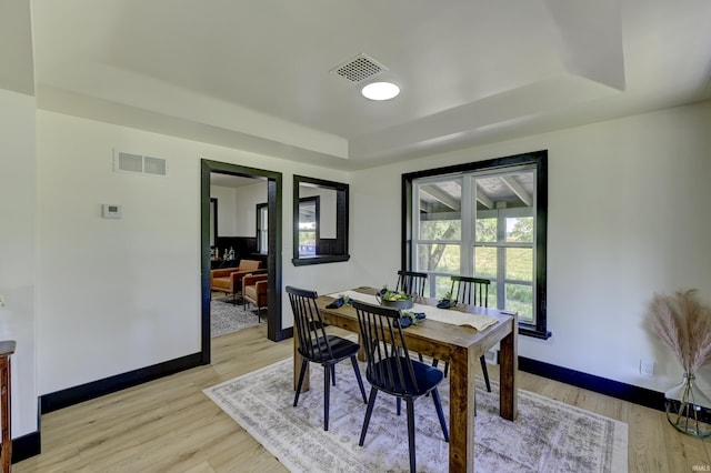 dining area with a raised ceiling and light wood-type flooring