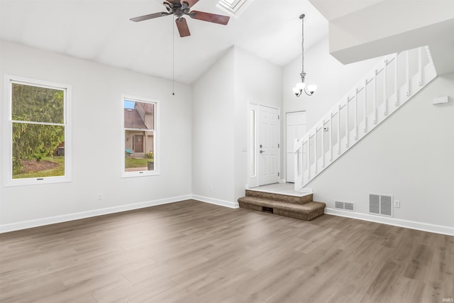 unfurnished living room featuring hardwood / wood-style flooring, ceiling fan with notable chandelier, and high vaulted ceiling