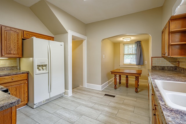 kitchen with vaulted ceiling, white refrigerator with ice dispenser, sink, and tasteful backsplash