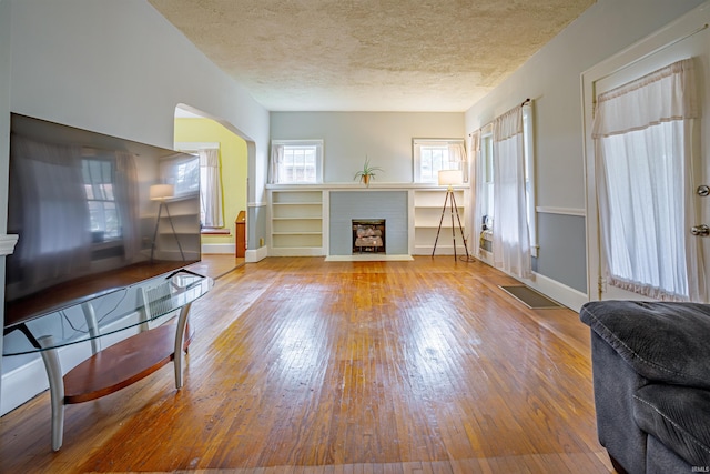 living room with hardwood / wood-style floors, a textured ceiling, and a brick fireplace