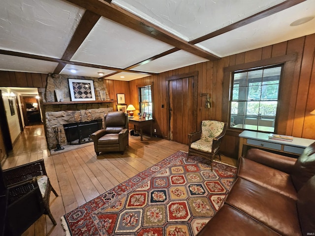 living room with beamed ceiling, light hardwood / wood-style flooring, a stone fireplace, and coffered ceiling