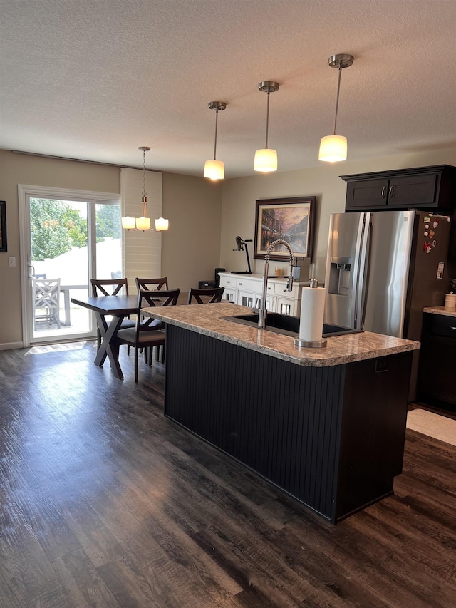 kitchen featuring stainless steel refrigerator with ice dispenser, dark hardwood / wood-style floors, pendant lighting, and an island with sink