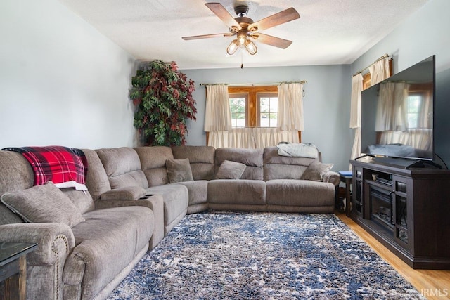 living room featuring a textured ceiling, a fireplace, light wood-type flooring, and ceiling fan