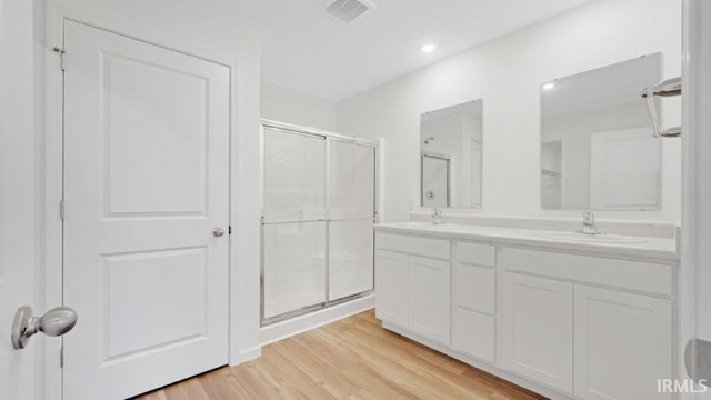 bathroom featuring double vanity, visible vents, a sink, a shower stall, and wood finished floors