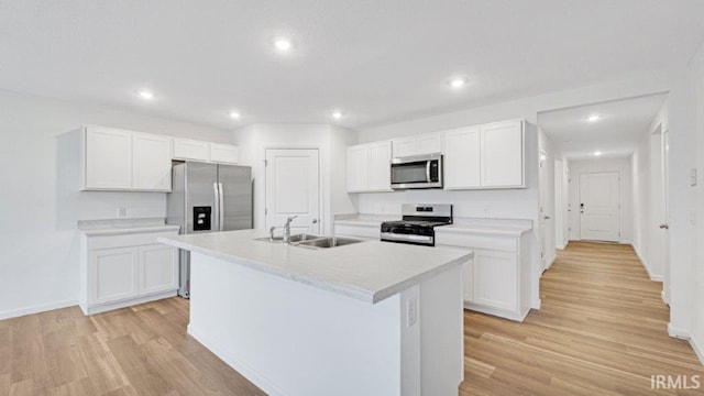 kitchen featuring stainless steel appliances, light countertops, white cabinets, a sink, and an island with sink