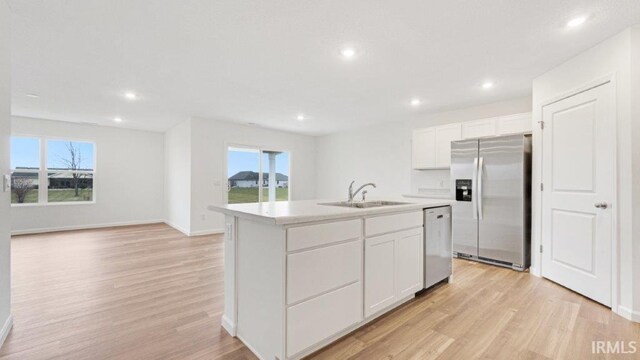 kitchen with an island with sink, stainless steel appliances, light countertops, white cabinetry, and a sink