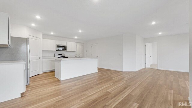 kitchen with light countertops, appliances with stainless steel finishes, light wood-style floors, white cabinets, and a kitchen island with sink