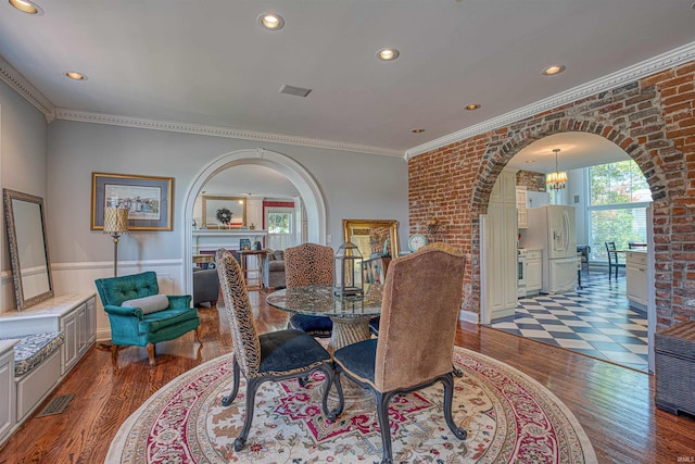 dining space with ornamental molding, brick wall, light hardwood / wood-style flooring, a notable chandelier, and a fireplace