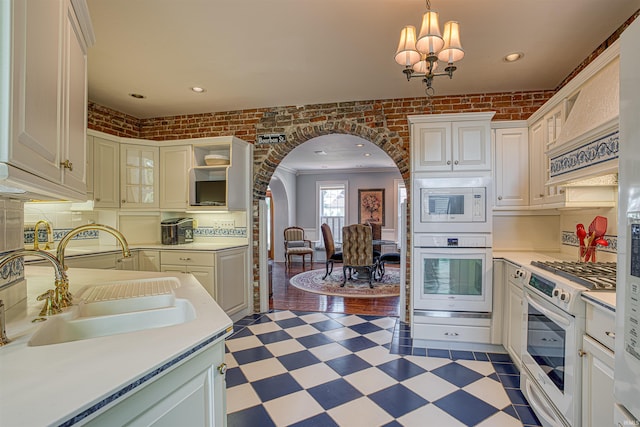 kitchen featuring brick wall, pendant lighting, white appliances, and sink