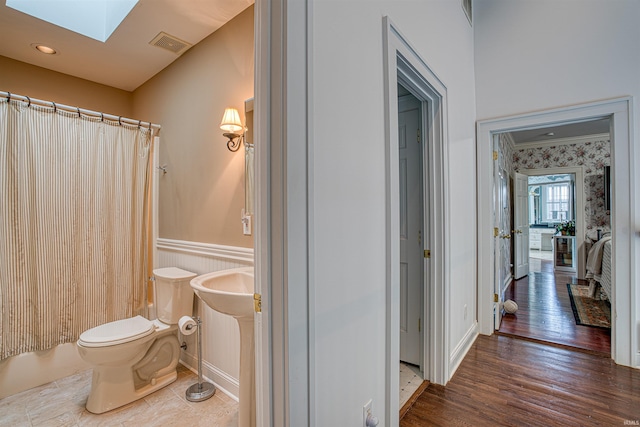 bathroom with a shower with shower curtain, hardwood / wood-style floors, a skylight, and toilet