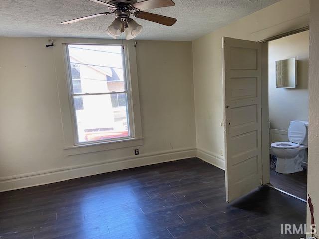 empty room featuring a textured ceiling, ceiling fan, a healthy amount of sunlight, and dark wood-type flooring