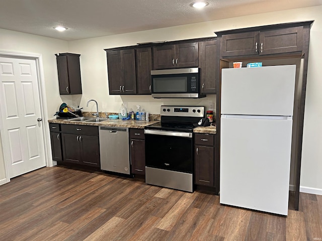 kitchen with light stone countertops, appliances with stainless steel finishes, dark brown cabinetry, dark wood-type flooring, and sink