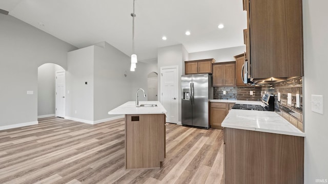 kitchen featuring sink, an island with sink, appliances with stainless steel finishes, tasteful backsplash, and decorative light fixtures