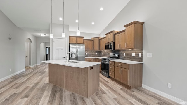 kitchen featuring sink, an island with sink, appliances with stainless steel finishes, tasteful backsplash, and decorative light fixtures