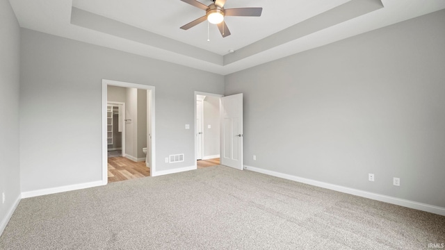 unfurnished bedroom featuring light carpet, a raised ceiling, and ceiling fan