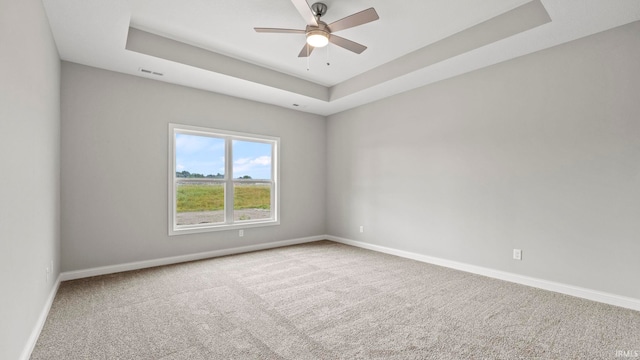 carpeted empty room with a raised ceiling and ceiling fan