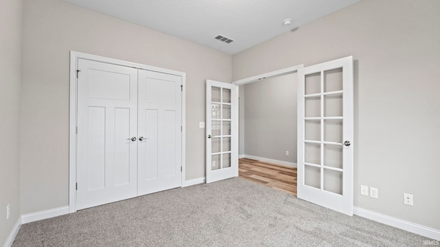 unfurnished bedroom with a closet, french doors, and light carpet