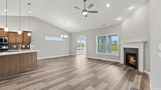 unfurnished living room featuring ceiling fan with notable chandelier, wood-type flooring, sink, and high vaulted ceiling