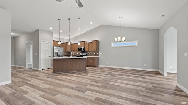 kitchen featuring pendant lighting, high vaulted ceiling, ceiling fan with notable chandelier, an island with sink, and stainless steel appliances