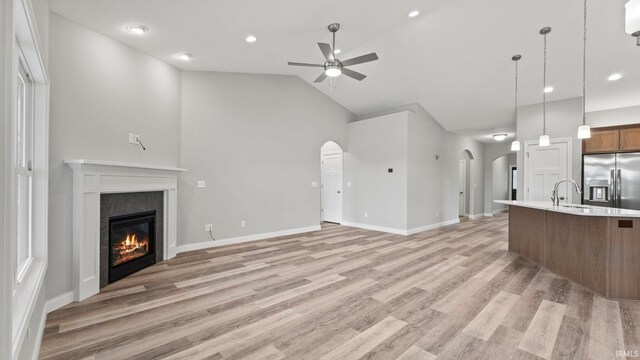 unfurnished living room with ceiling fan, light hardwood / wood-style floors, sink, and high vaulted ceiling