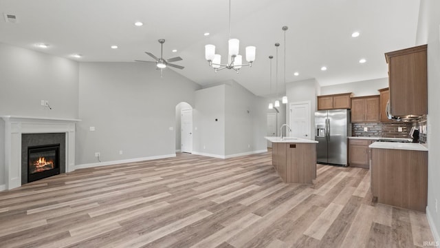 kitchen featuring stainless steel refrigerator with ice dispenser, backsplash, ceiling fan with notable chandelier, hanging light fixtures, and an island with sink