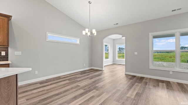 unfurnished dining area with ceiling fan with notable chandelier, light hardwood / wood-style floors, and lofted ceiling