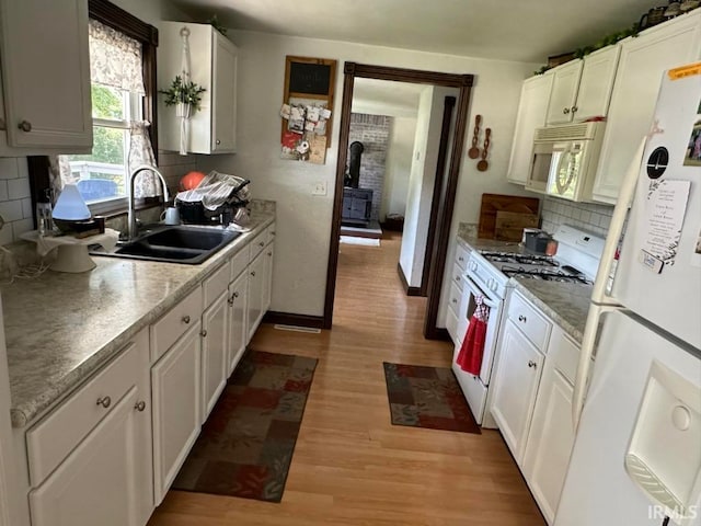 kitchen featuring white cabinetry, sink, a wood stove, light wood-type flooring, and white appliances