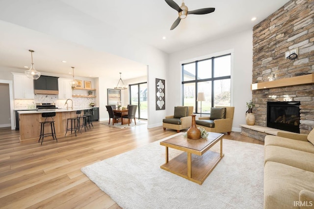 living room with ceiling fan, light hardwood / wood-style floors, a stone fireplace, and sink