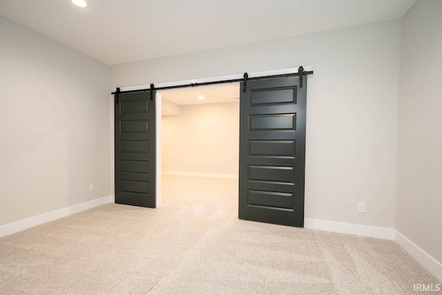 unfurnished bedroom with a barn door and light carpet