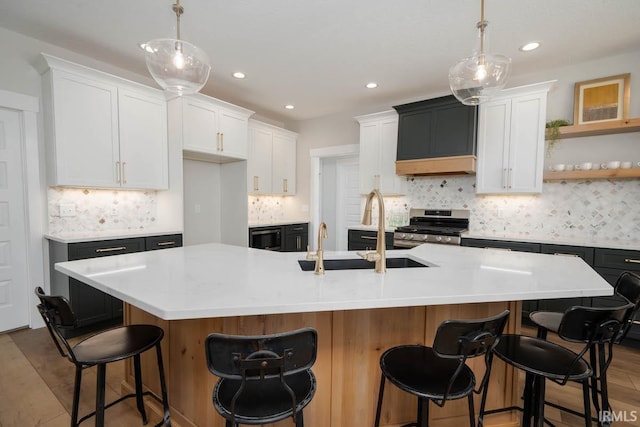 kitchen featuring a breakfast bar, white cabinetry, a kitchen island with sink, and stainless steel range