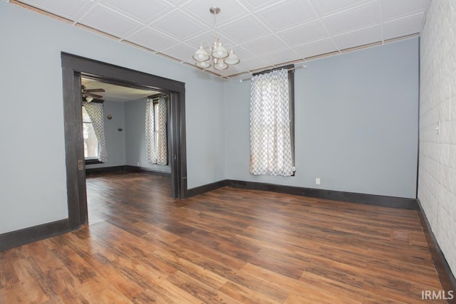 unfurnished room with ceiling fan with notable chandelier, a healthy amount of sunlight, and dark hardwood / wood-style flooring