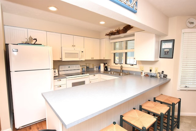 kitchen with white appliances, white cabinetry, sink, kitchen peninsula, and a breakfast bar area