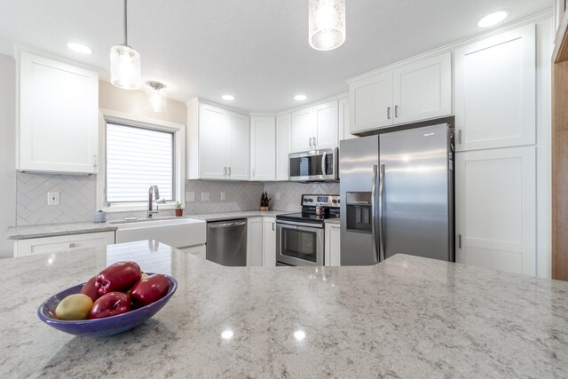 kitchen featuring tasteful backsplash, stainless steel appliances, light stone counters, decorative light fixtures, and white cabinetry