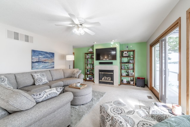 living room featuring light carpet, ceiling fan, a tiled fireplace, and visible vents