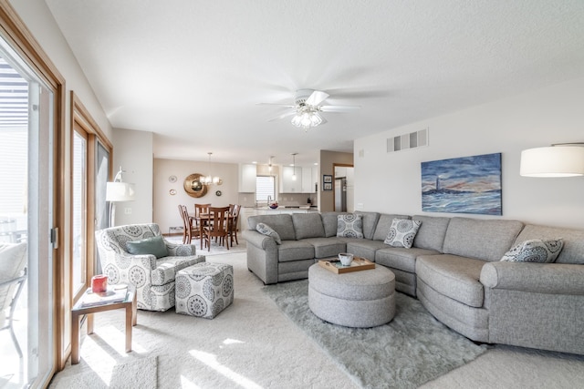 living area with ceiling fan with notable chandelier, visible vents, and light colored carpet