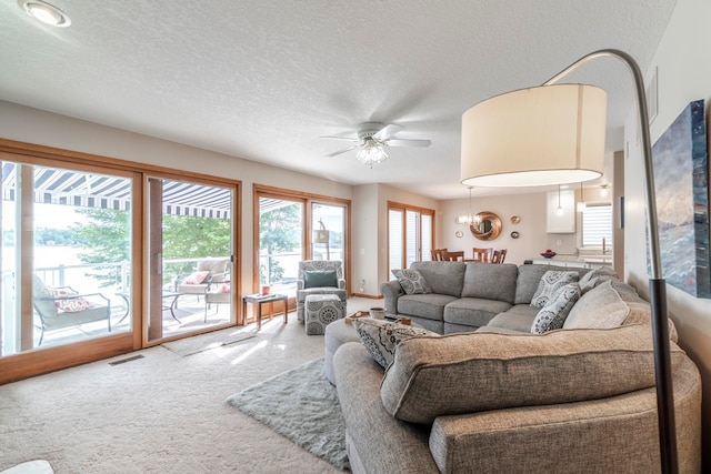 living room with a textured ceiling, carpet floors, and ceiling fan