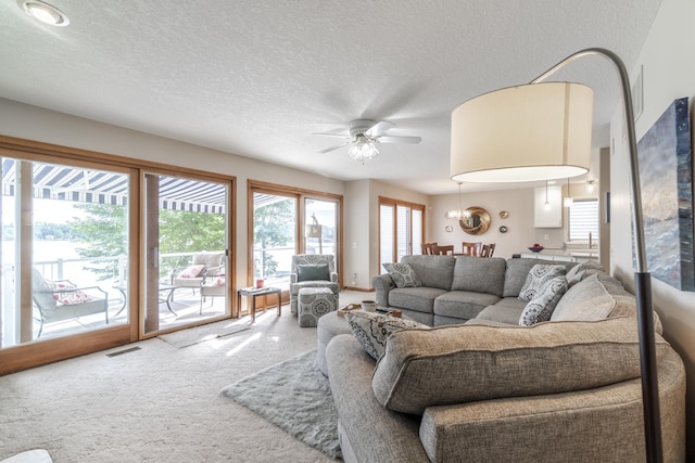 living area featuring a ceiling fan, visible vents, a textured ceiling, and carpet flooring