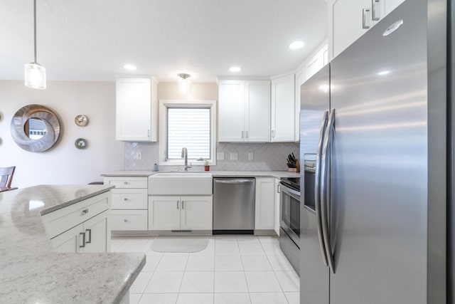 kitchen with hanging light fixtures, appliances with stainless steel finishes, white cabinetry, a sink, and light stone countertops