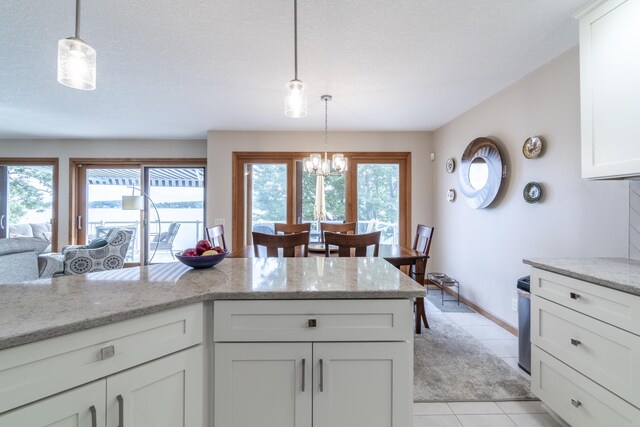 kitchen with pendant lighting, light stone counters, light tile patterned floors, a chandelier, and white cabinetry