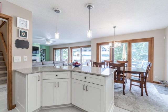 kitchen with light stone counters, open floor plan, hanging light fixtures, a fireplace, and white cabinetry