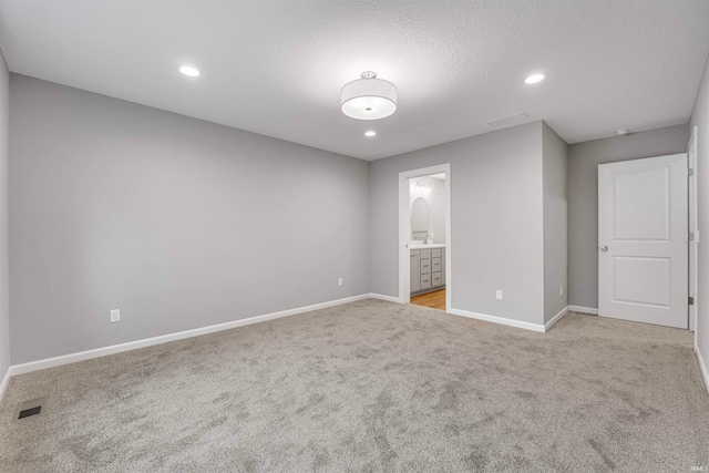 unfurnished bedroom with a textured ceiling, ensuite bathroom, and light colored carpet