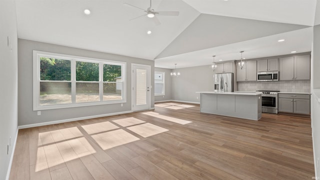 kitchen with appliances with stainless steel finishes, light wood-type flooring, pendant lighting, gray cabinets, and a kitchen island with sink