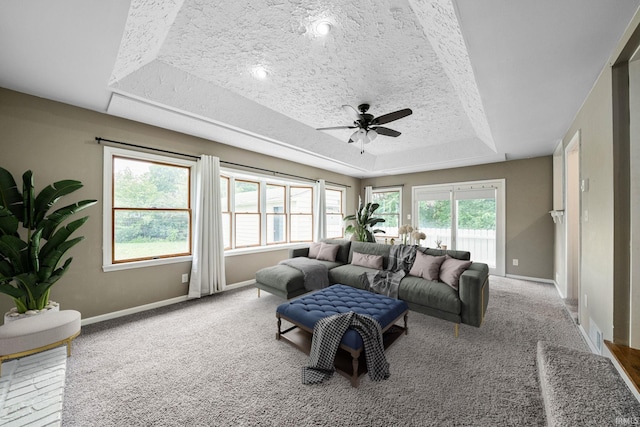 carpeted living room featuring ceiling fan, a textured ceiling, and a tray ceiling