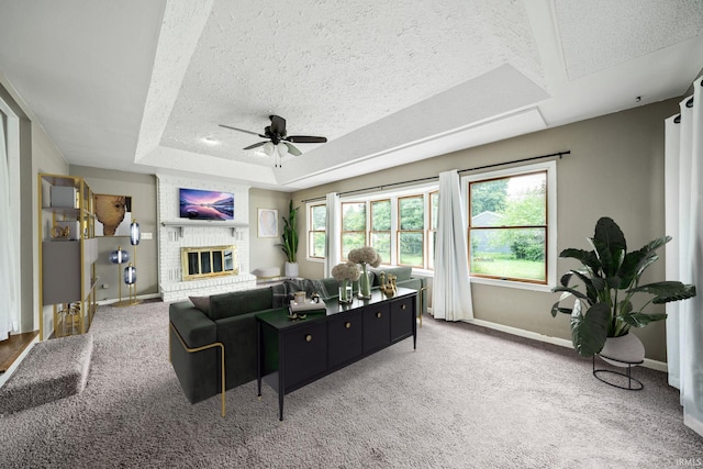 carpeted living room with a textured ceiling, a brick fireplace, ceiling fan, and a raised ceiling