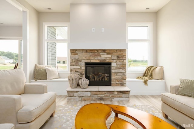 sitting room with a stone fireplace, hardwood / wood-style floors, and plenty of natural light