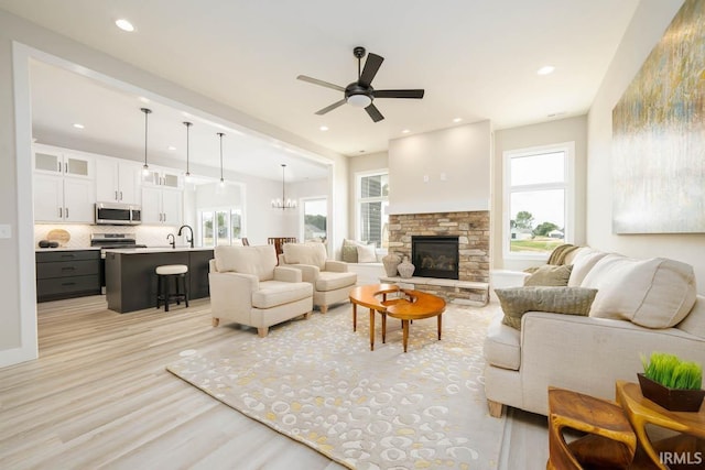 living room with a fireplace, ceiling fan with notable chandelier, light hardwood / wood-style flooring, and plenty of natural light