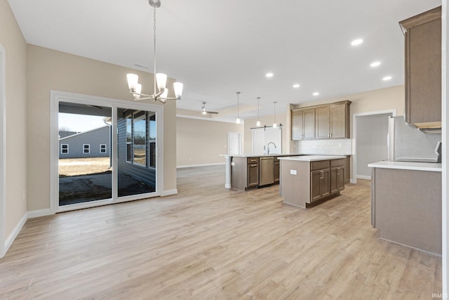 kitchen with hanging light fixtures, a center island with sink, dishwasher, light hardwood / wood-style floors, and backsplash