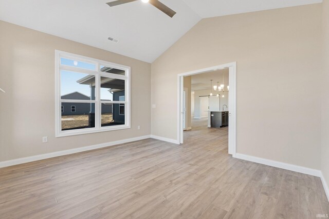 unfurnished room with high vaulted ceiling, ceiling fan with notable chandelier, and light hardwood / wood-style flooring