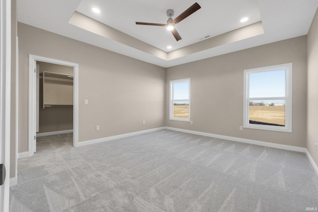 unfurnished bedroom featuring a raised ceiling, a spacious closet, light colored carpet, and ceiling fan