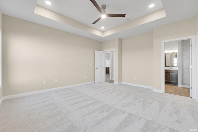 unfurnished bedroom with light carpet, connected bathroom, a raised ceiling, and ceiling fan